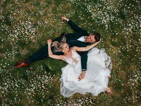 Luftaufnahme eines Brautpaars in einer Blumenwiese an seinem Hochzeitstag — DrohnXit Eventbegleitung